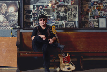 Tommy Shannon sitting on bench with guitar